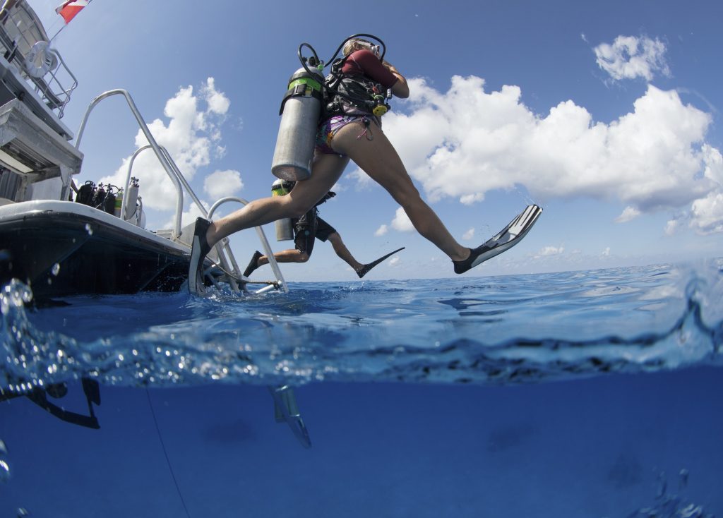 Scuba divers enter water leaping with a giant stride from a dive boat.