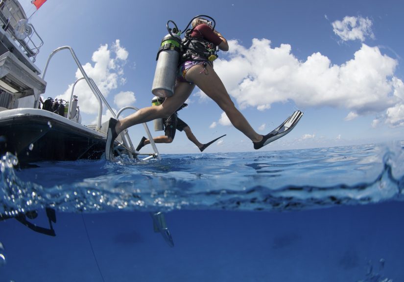 Scuba divers enter water leaping with a giant stride from a dive boat.